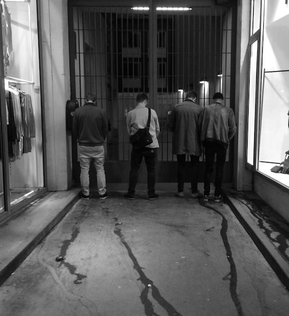 A black and white photo depicting FBI agents collecting evidence at Dealey Plaza in Dallas, Texas, immediately following the assassination of President John F. Kennedy, with bystanders looking on.